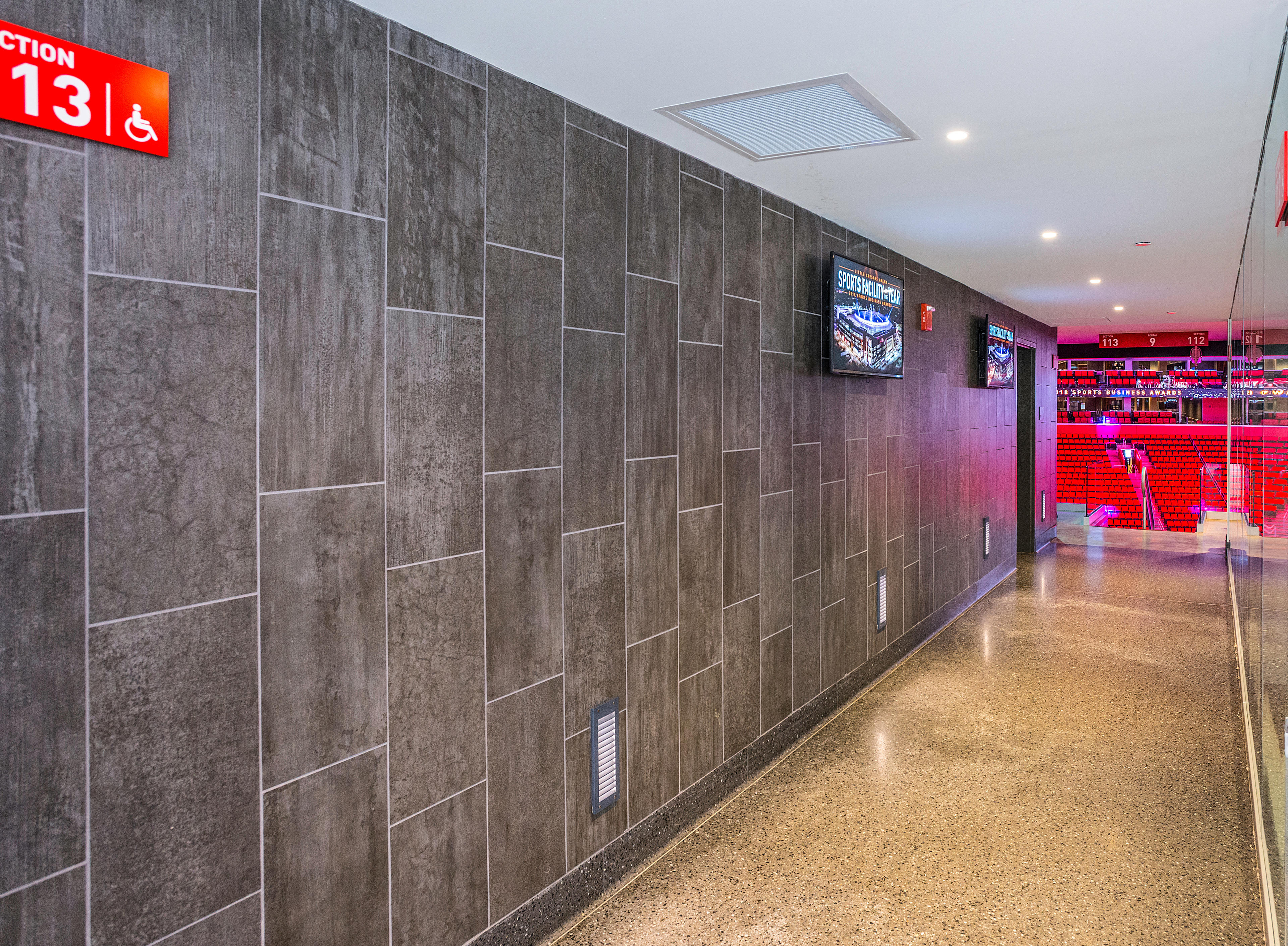 Pasillo con paredes grises de la arena Little Caesars y pantallas informativas.
