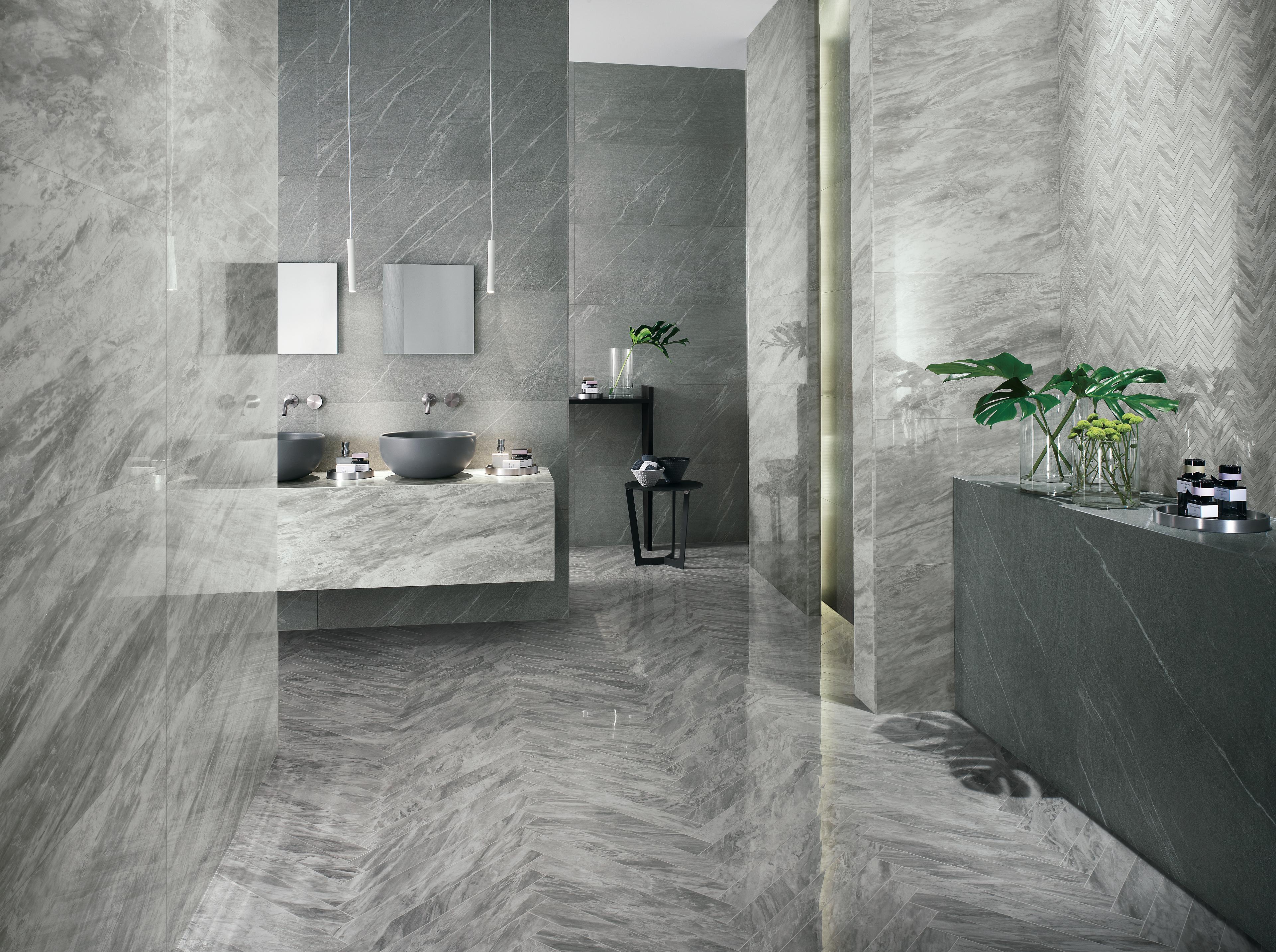 Salle de bain élégante avec carrelage gris, deux lavabos ronds, miroirs suspendus et détails de plantes vertes.
