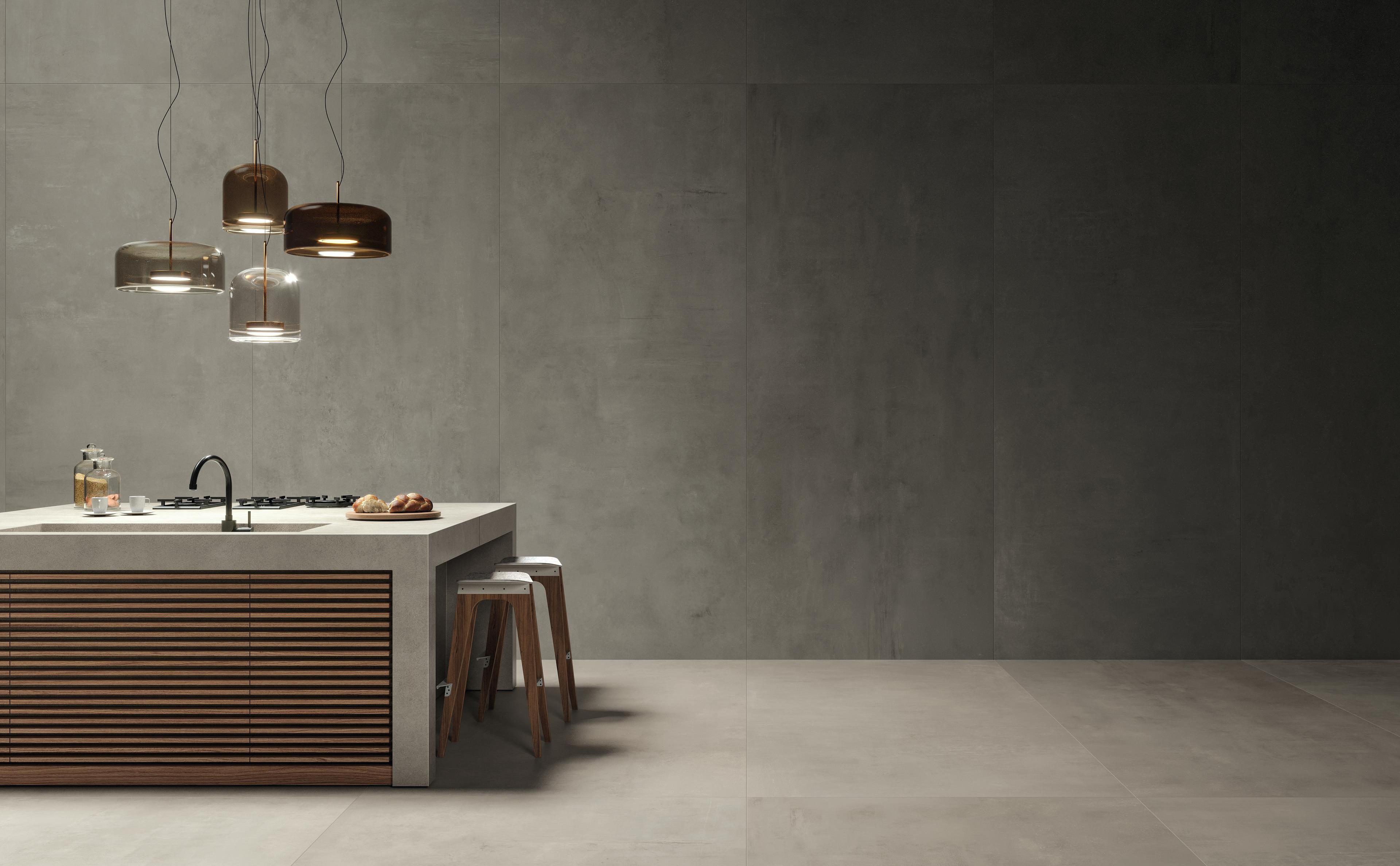 Cucina moderna con isola centrale e sgabelli, pavimento e pareti in ceramica Atlas Concorde Boost, illuminata da eleganti lampade a sospensione.