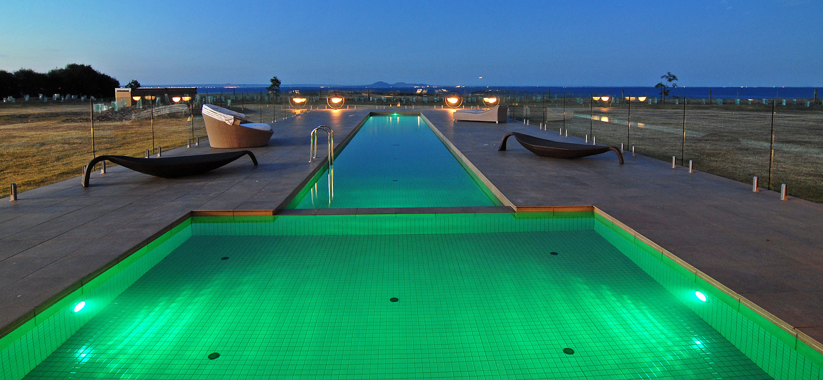 Piscine extérieure éclairée au coucher du soleil d’une villa privée en Australie, avec des chaises longues et une vue panoramique sur la mer.