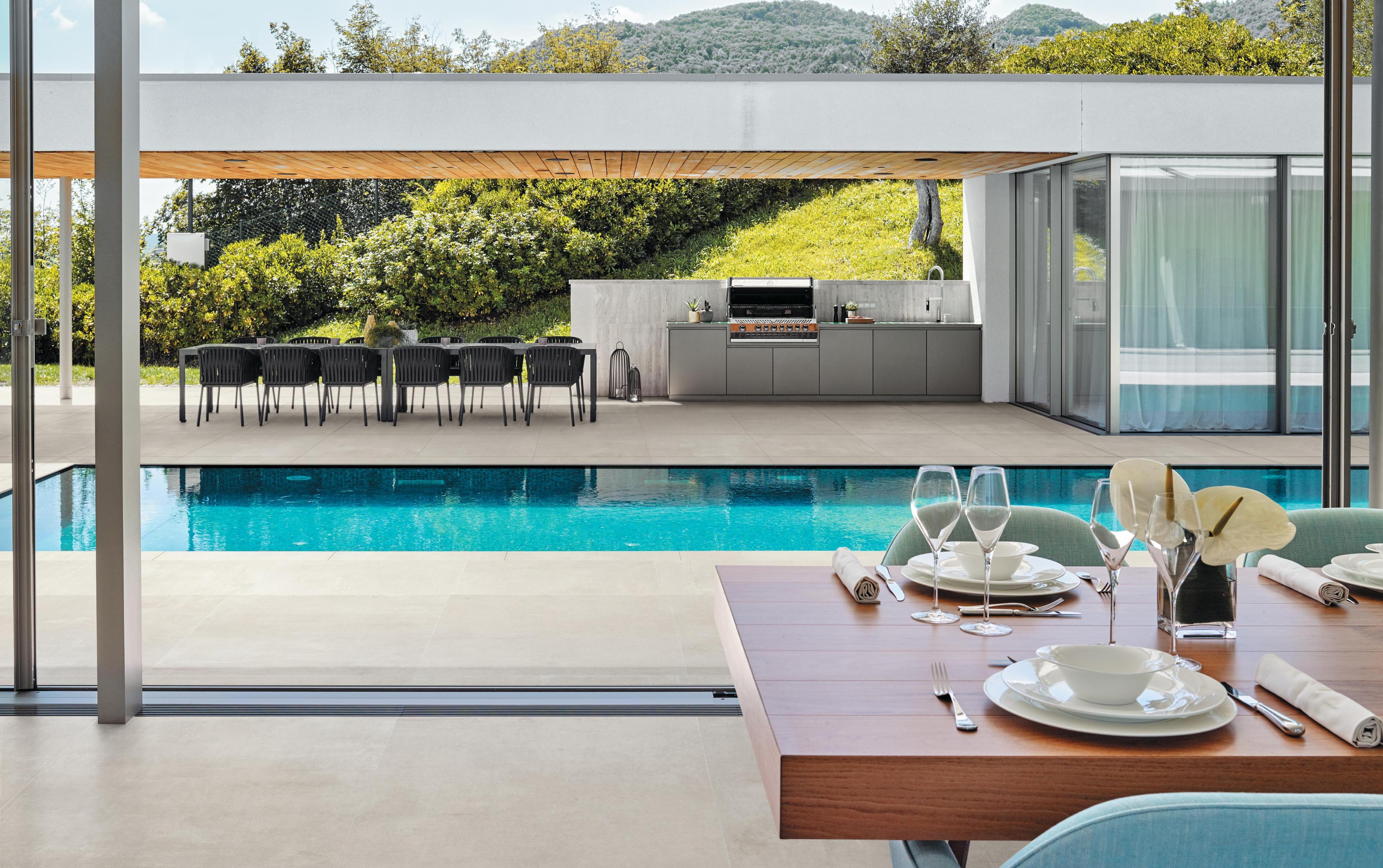 Elegante spazio esterno con pavimento in ceramica Atlas Concorde Boost, piscina, zona pranzo all'aperto e circondata da verde.