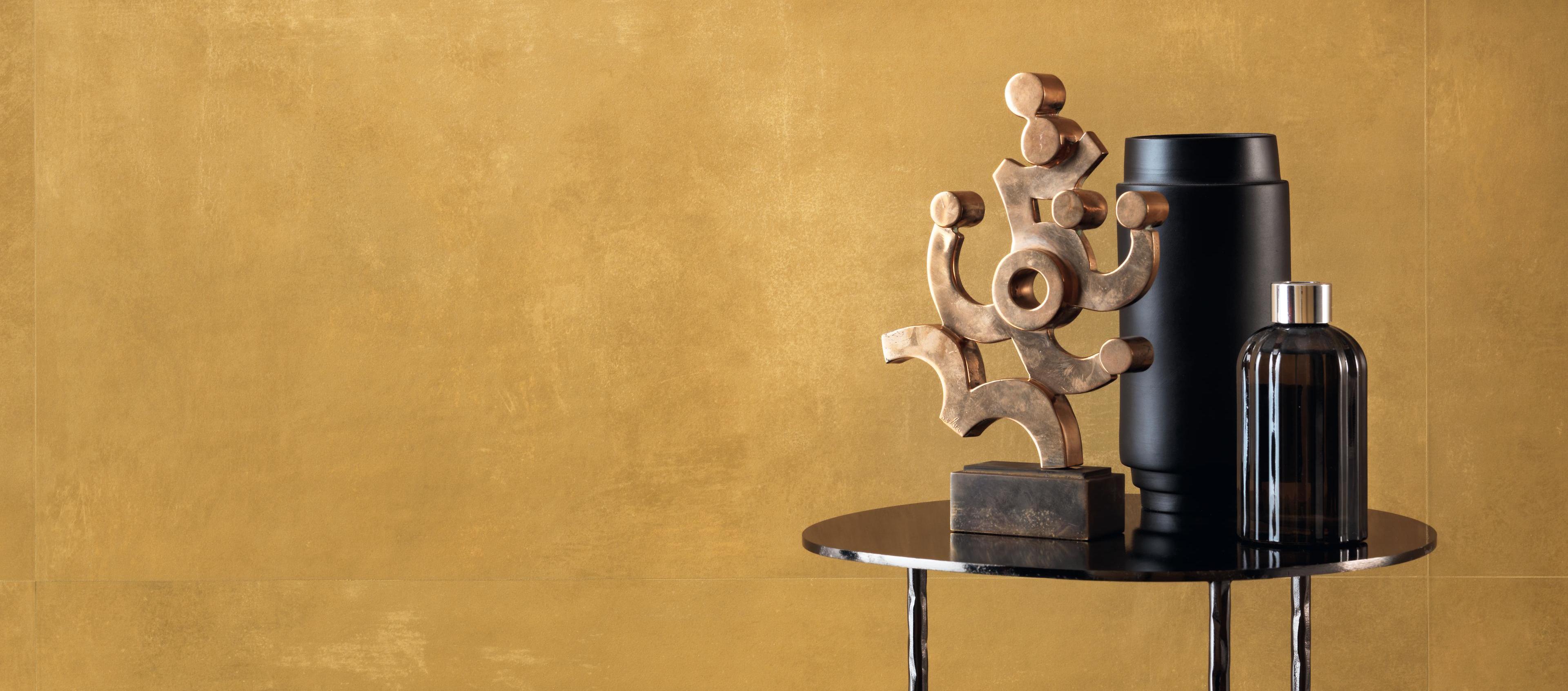 Wall covered with yellow cement tiles, decorated with a wooden sculpture and a black vase on a coffee table. 