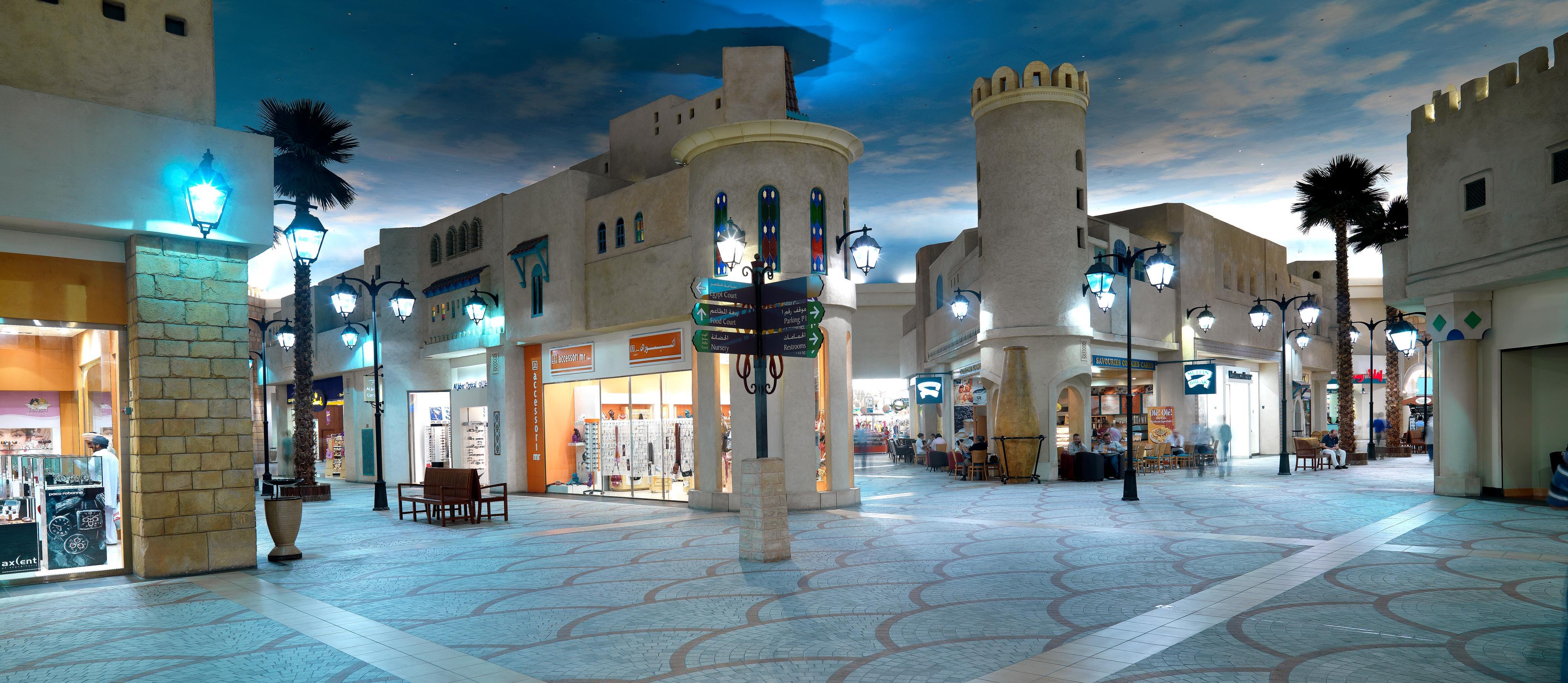 Vista interior del Ibn Battuta Mall, caracterizada por suelos decorados con motivos geométricos, una fachada arquitectónica de estilo tradicional que evoca el ambiente de una antigua ciudad árabe.