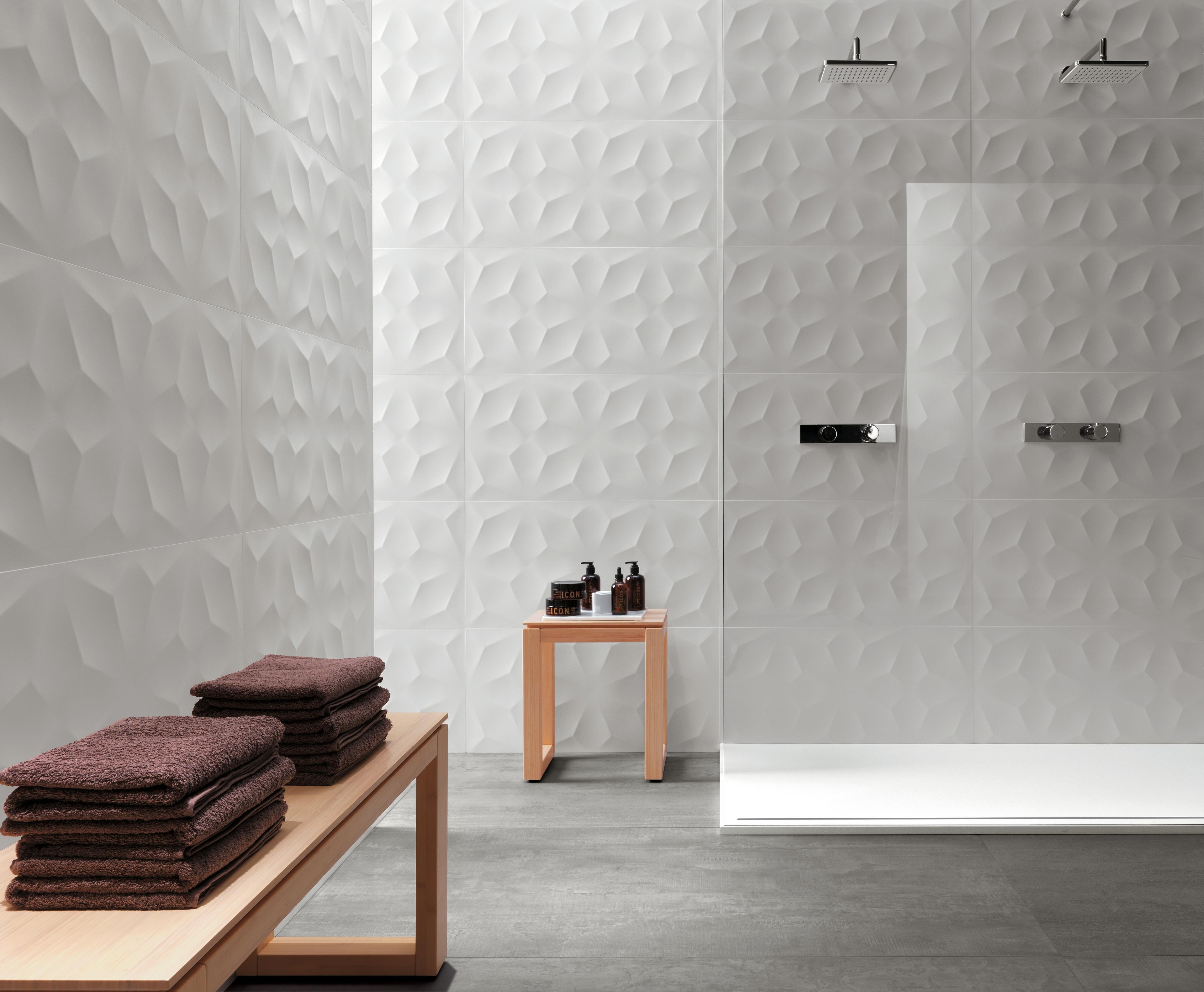 Bagno con rivestimento piastrelle 3D bianche dal design geometrico, doccia moderna e tavolino con prodotti da bagno.