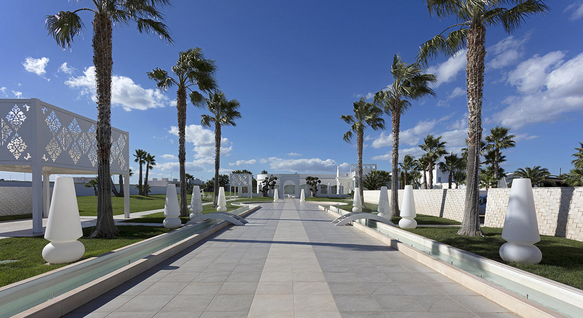 Avenue pavée de palmiers et de sculptures blanches, menant à l’élégant bâtiment Pietra Perla de Sannicandro di Bari