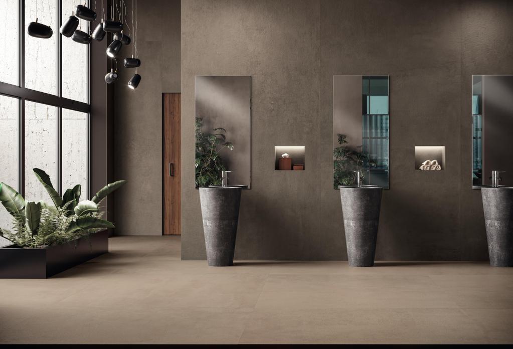 Baño moderno con suelo y paredes de cerámica Atlas Concorde Boost Pro, lavabos cilíndricos de piedra, grandes espejos rectangulares y plantas decorativas cerca de una ventana panorámica.