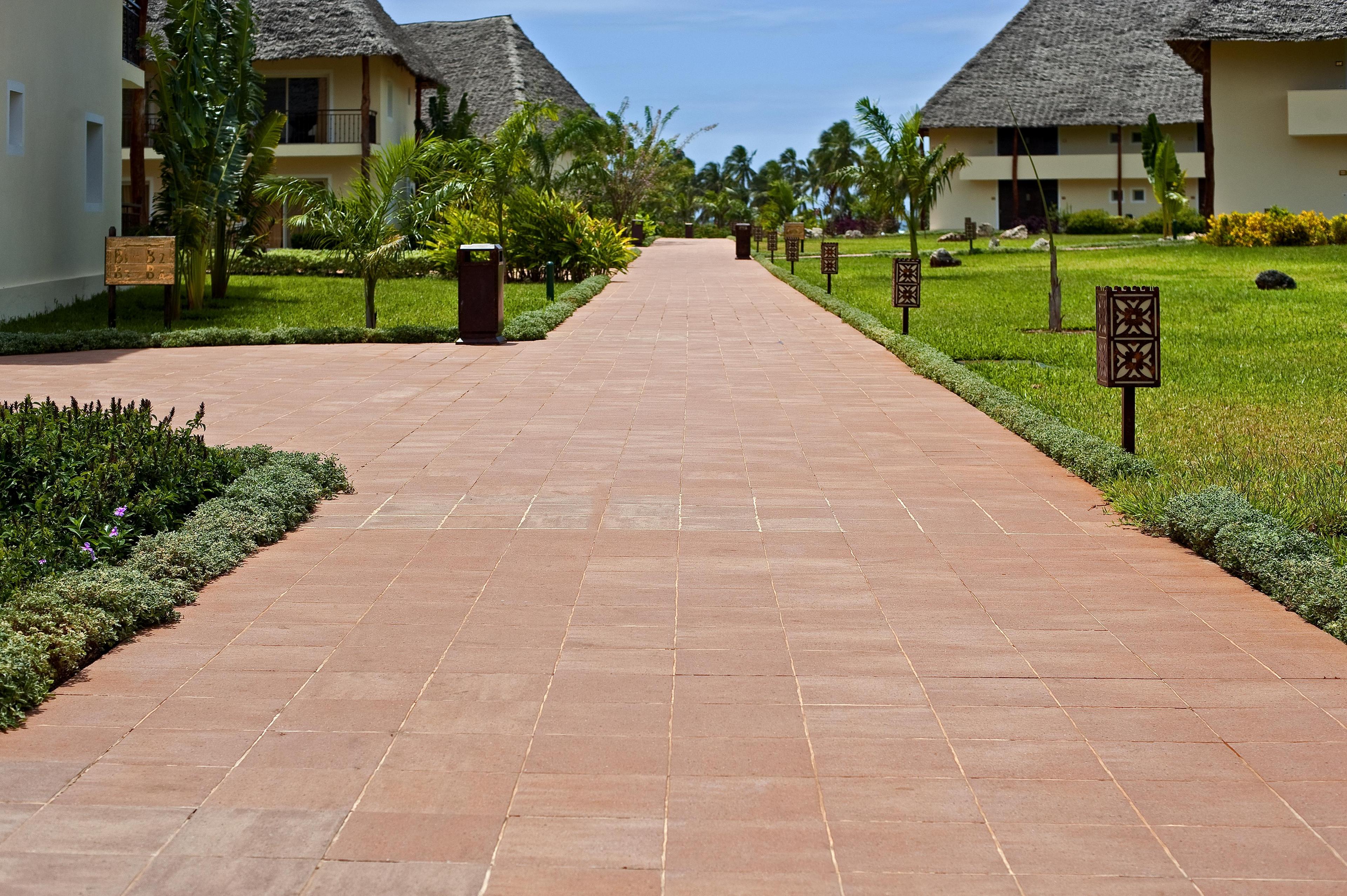Paved trail in the Diamond Dream resort of Zanzibar, surrounded by manicured gardens and buildings with thatched roofs.