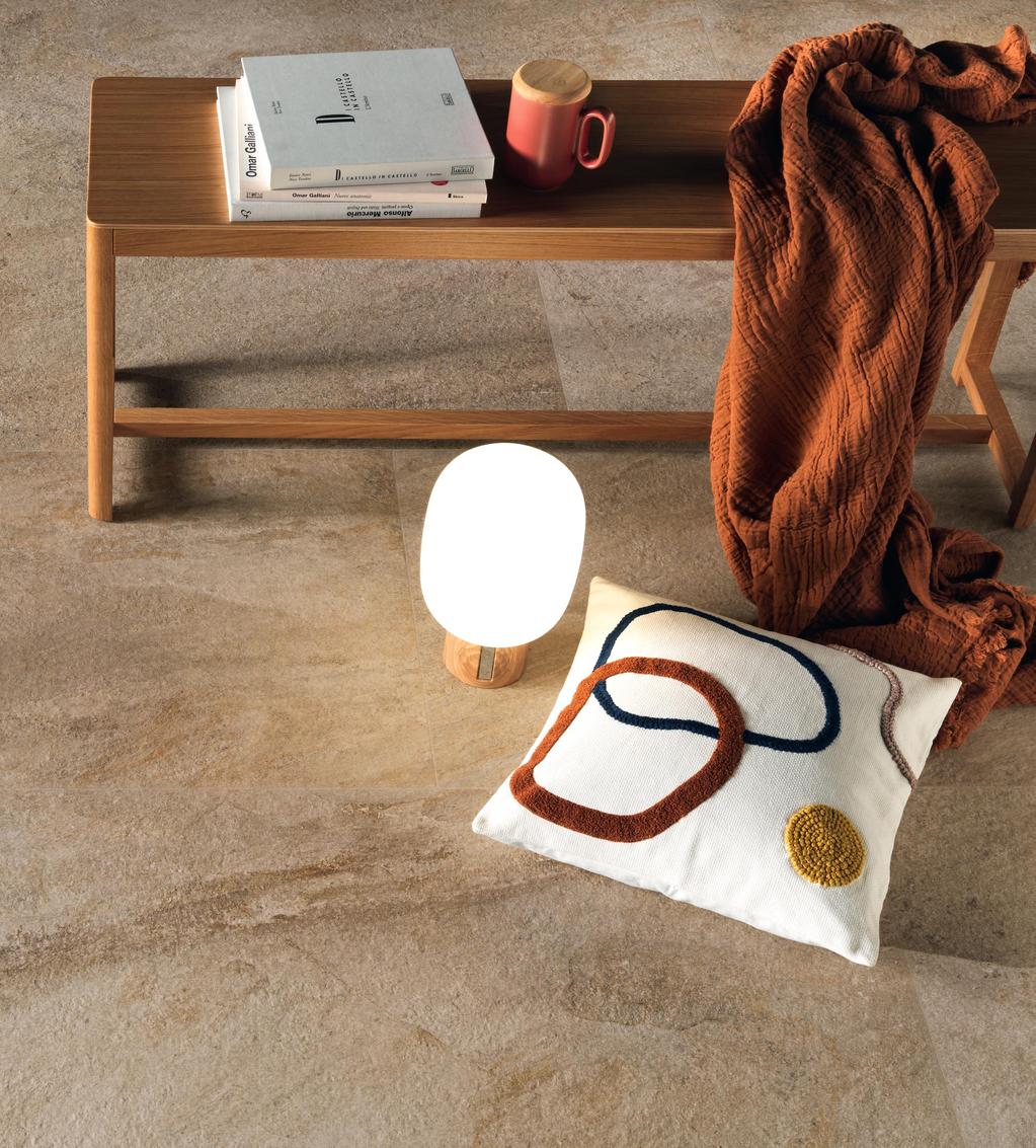 Floor with beige tiles with golden veins, furnished with a wooden table on which are resting books and a red cup. 