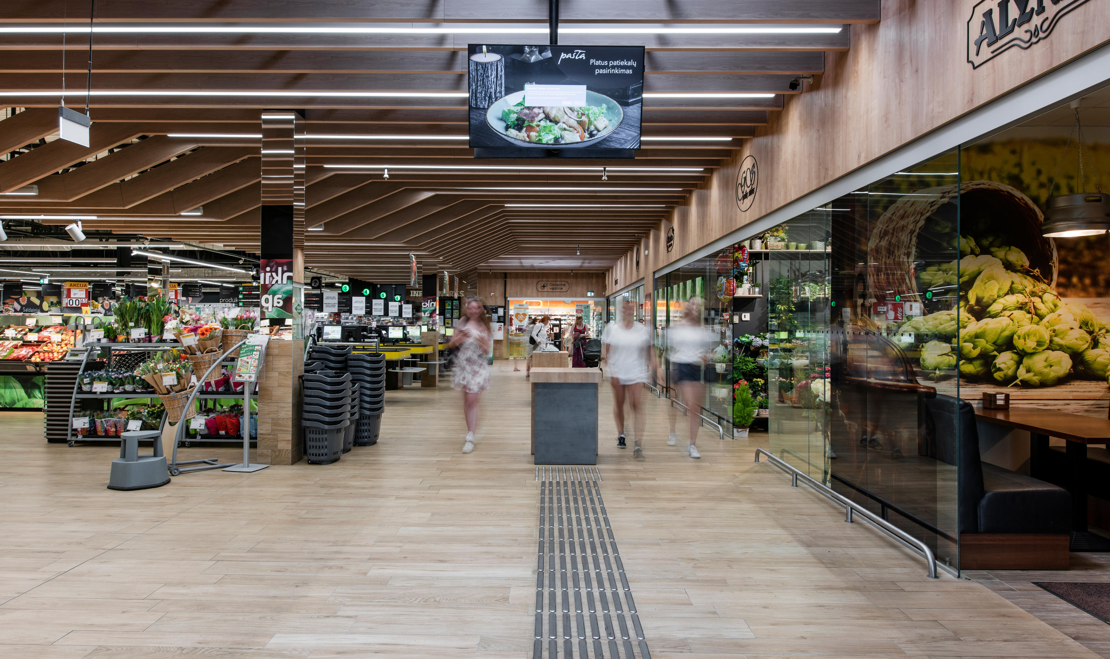 Интерьер супермаркета с полками, заполненными свежими продуктами, тележками и покупателями, идущими по проходу.