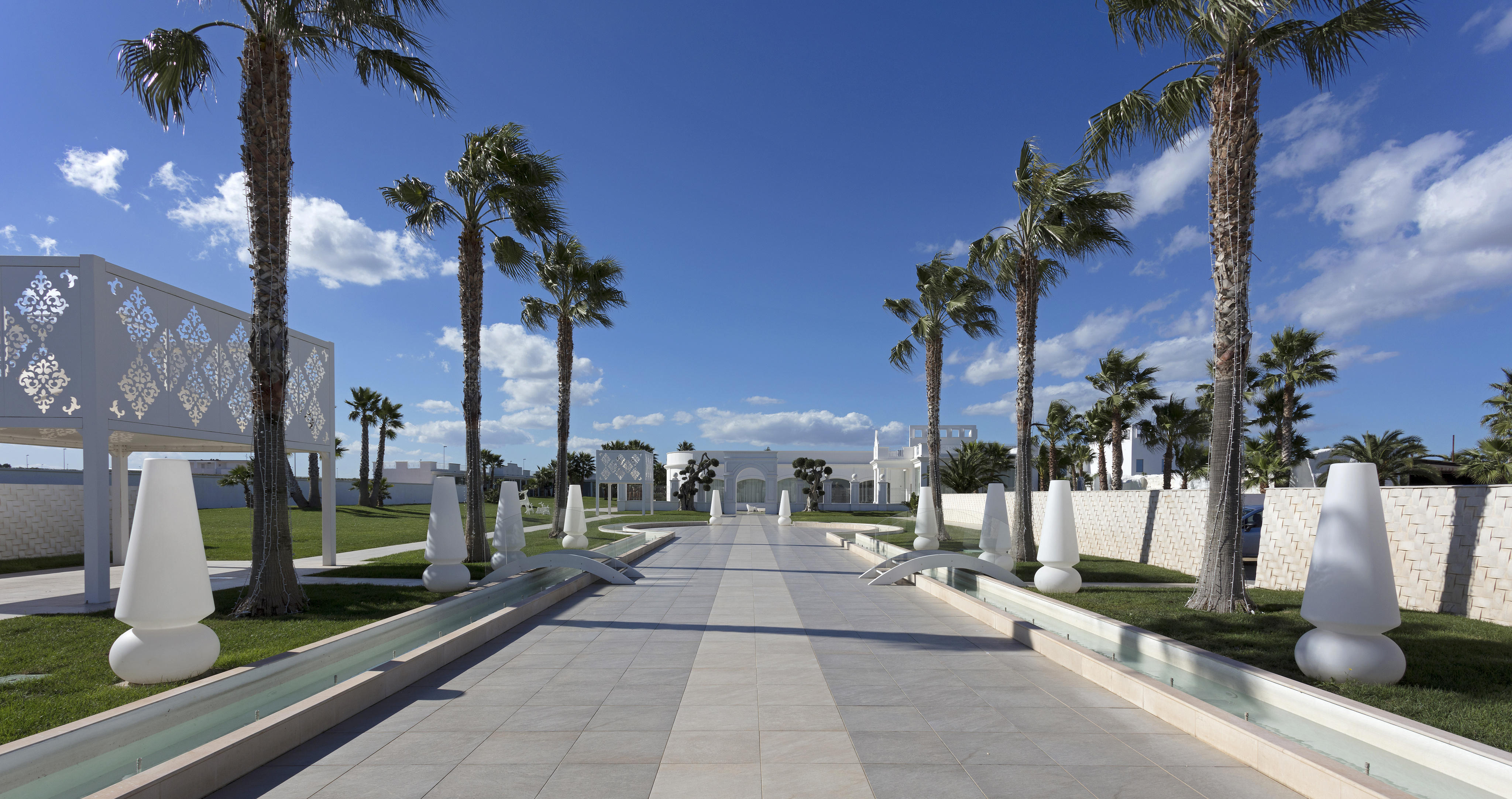 Avenue pavée de palmiers et de sculptures blanches, menant à l’élégant bâtiment Pietra Perla de Sannicandro di Bari.