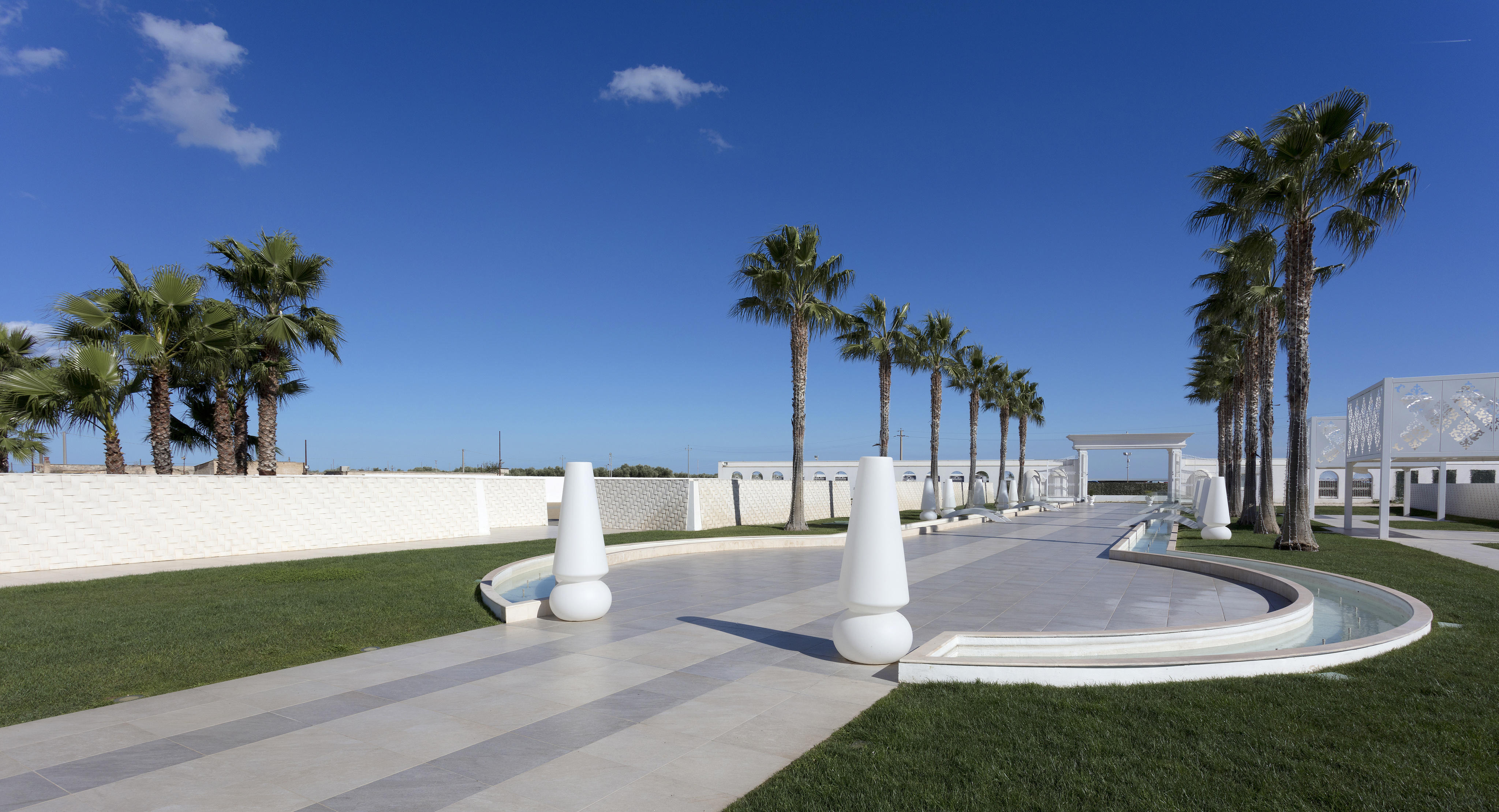 Avenue en pierre avec des palmiers et des sculptures blanches, situé à l’édifice Pietra Perla de Sannicandro di Bari.