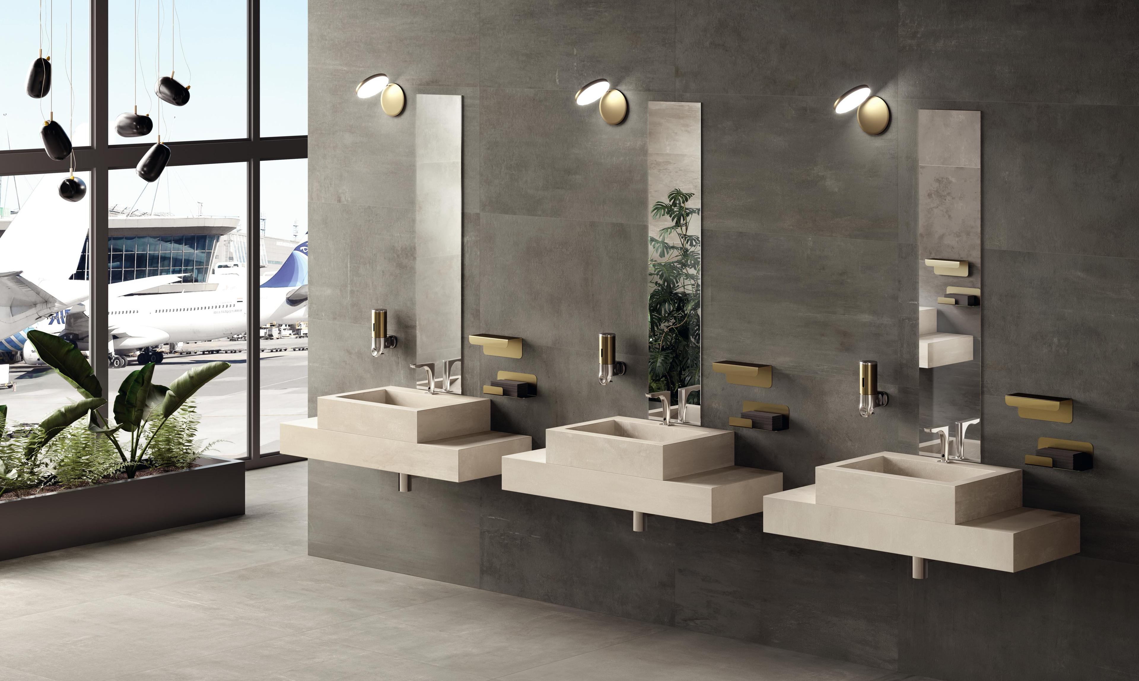 Modernes Badezimmer am Flughafen mit drei Waschbecken aus Feinsteinzeug, großen vertikalen Spiegeln und Seifenautomaten.