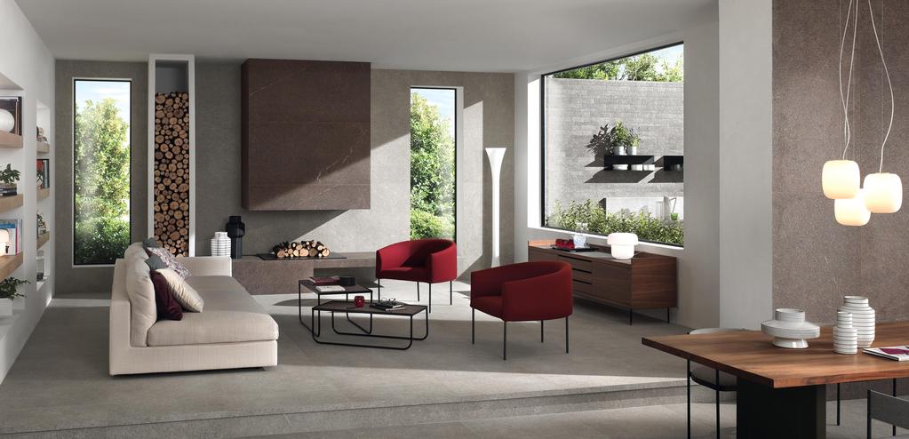 Geräumiges Wohnzimmer mit grauen Fliesen, beige Sofa, roten Stühlen, Kamin und großen Fenstern mit Blick auf den Garten.