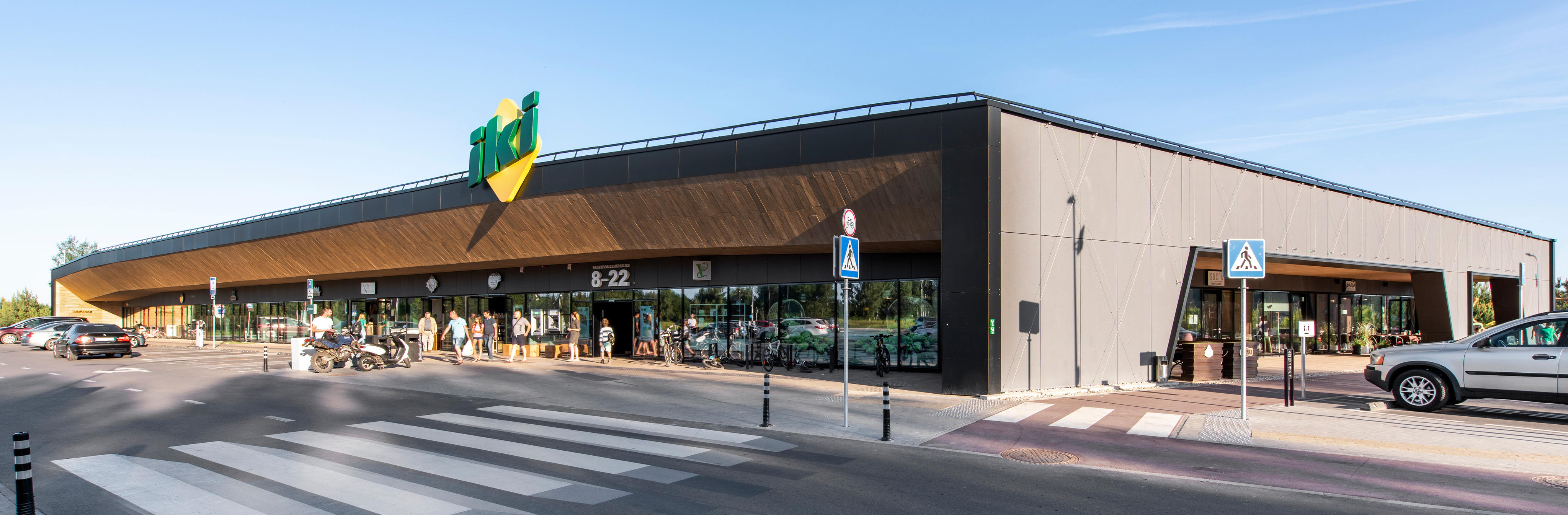 Esterno di un supermercato moderno con un ampio parcheggio e un attraversamento pedonale di fronte all'ingresso principale.