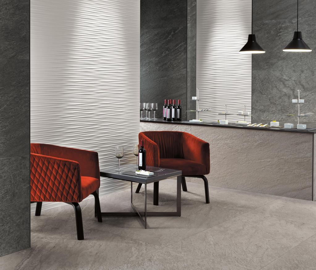 Elegante interno con pavimento e pareti in gres porcellanato Atlas Concorde Brave. Due poltrone rosse sono disposte attorno a un tavolino, con bottiglie di vino sul bancone sullo sfondo.