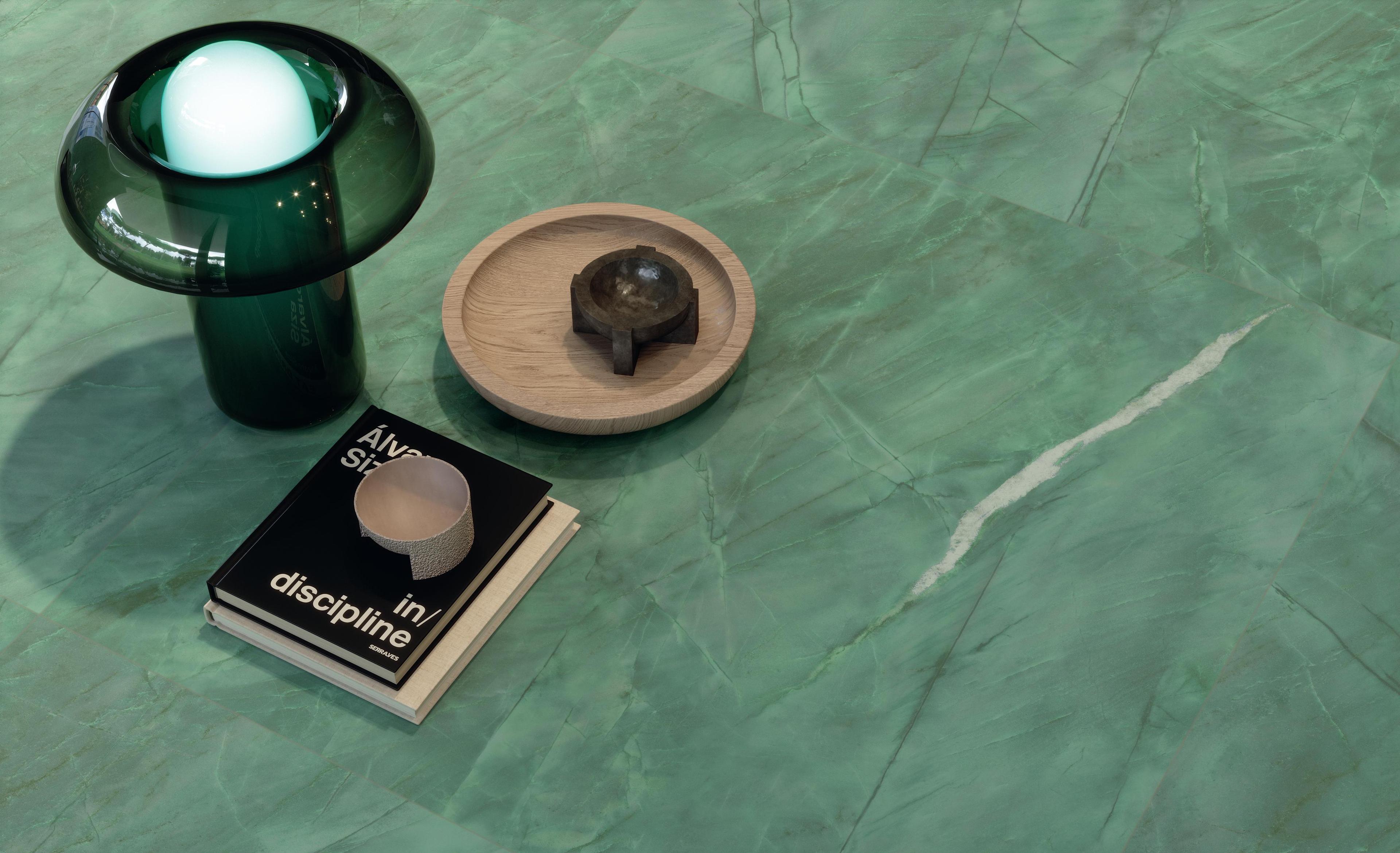 Detalle de suelo en gres porcelánico verde con encima libros y pequeños objetos decorativos. 