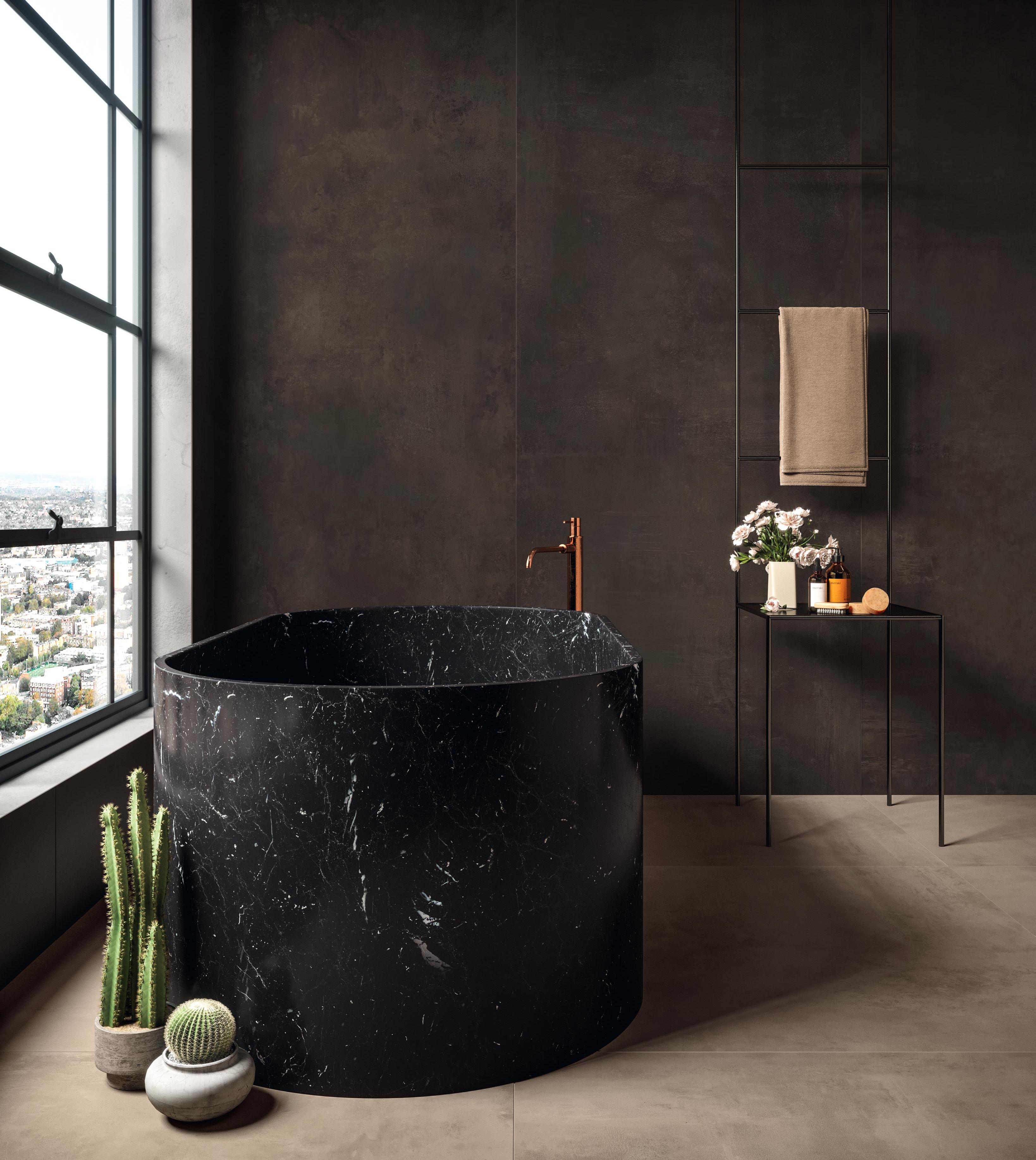 Elegant bathroom with large format tiles in brown concrete effect, with a round black marble bathtub and a small table with decorations.
