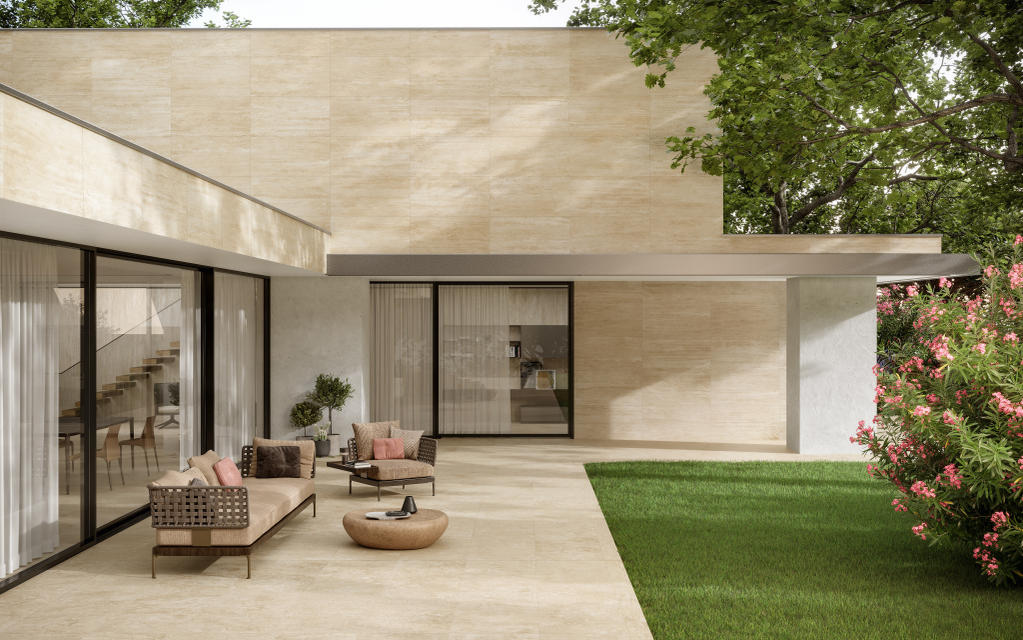 Exterior of a house with travertine floor and walls, outdoor seating area with woven furniture and green lawn. 