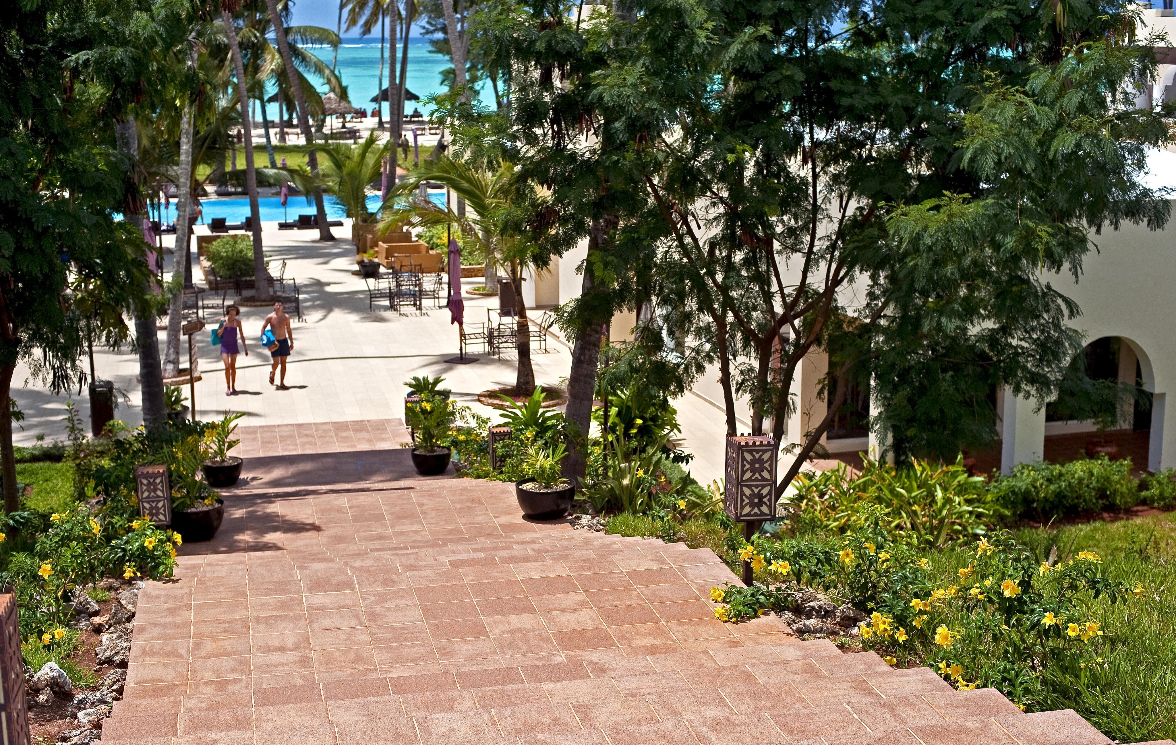 Tiled staircase leading to the swimming pool of the Diamond Dream resort in Zanzibar, surrounded by tropical gardens and palm trees, with sea views.
