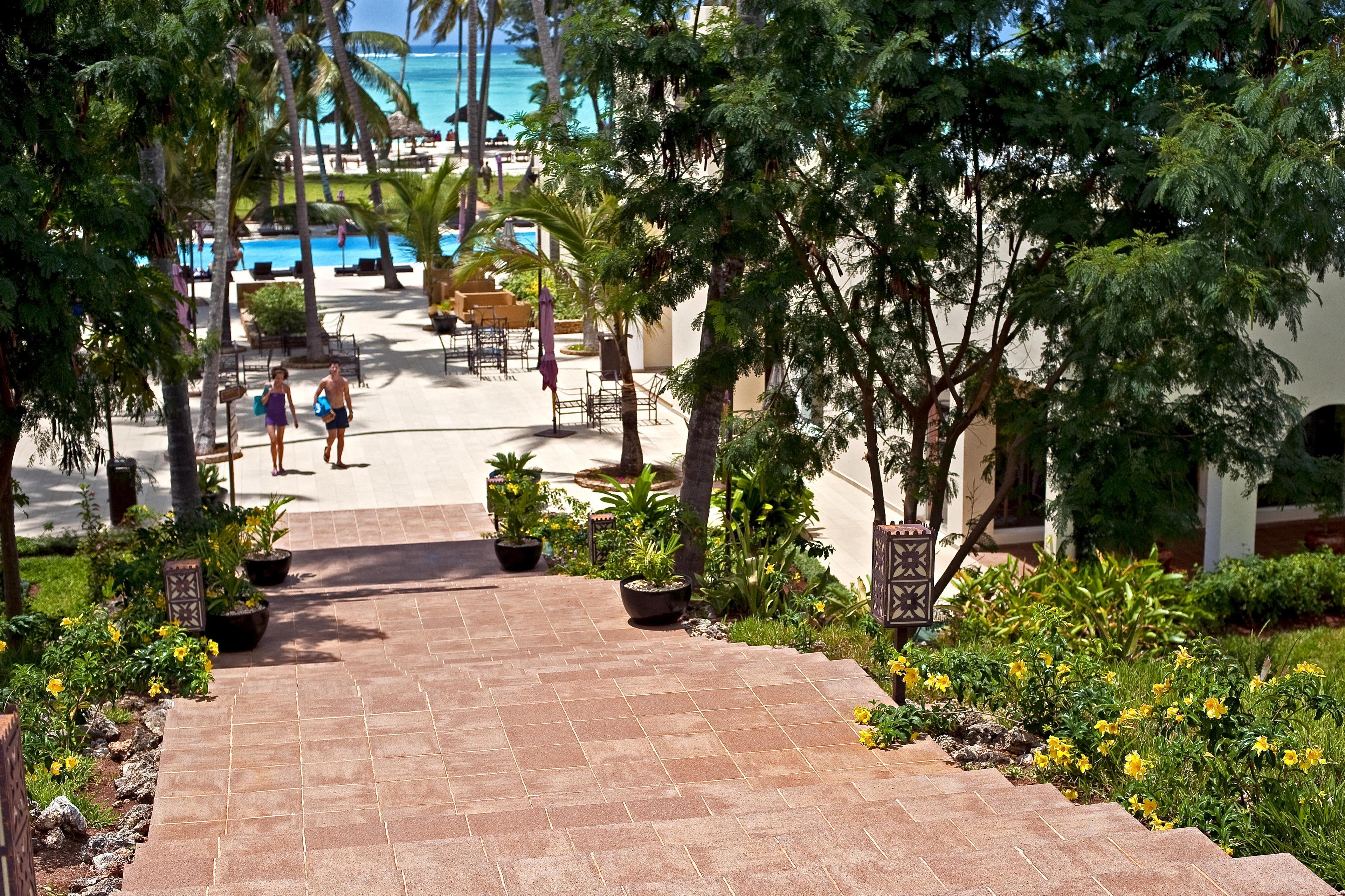 Tiled staircase leading to the swimming pool of the Diamond Dream resort in Zanzibar, surrounded by tropical gardens and palm trees, with sea views.
