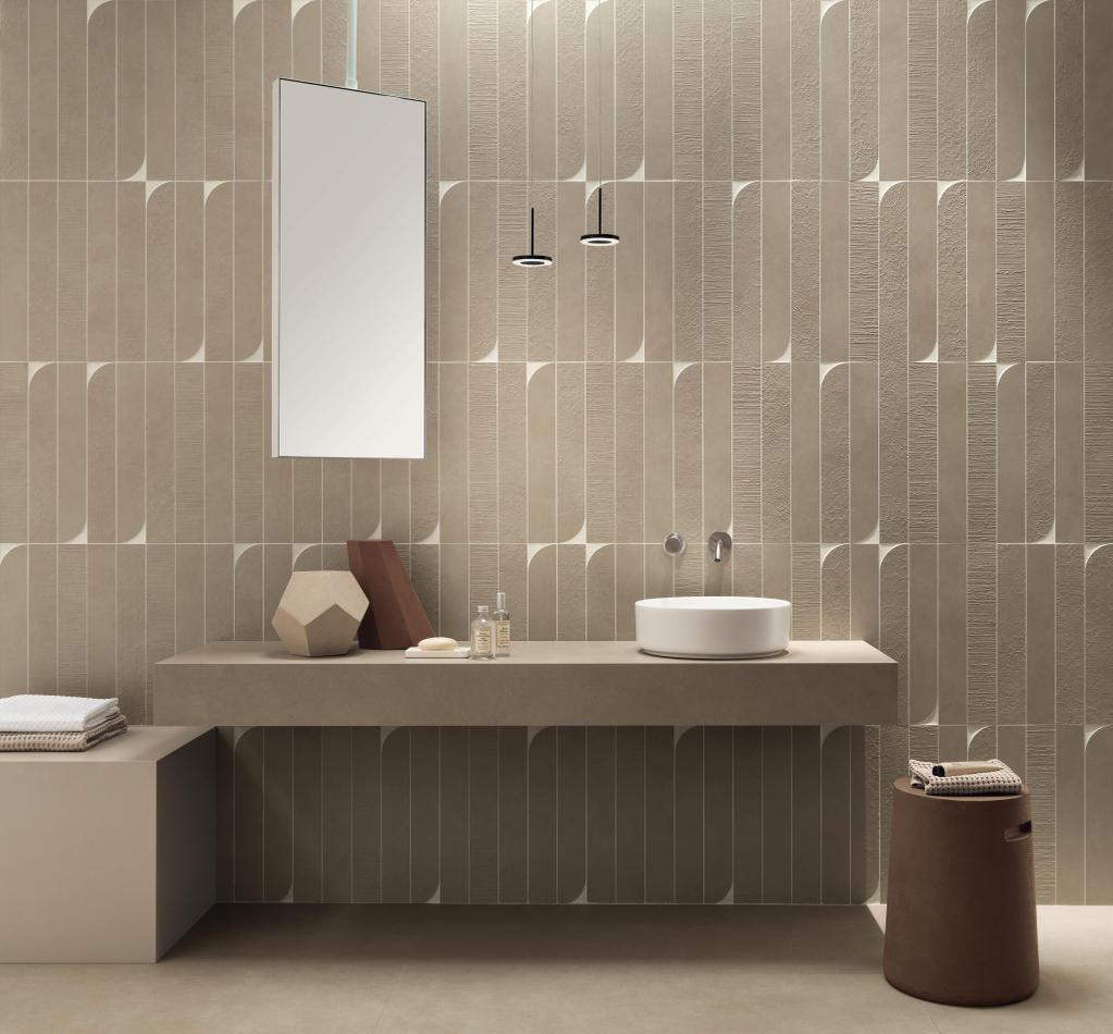 Elegante bagno con mosaico per il bagno beige, lavabo bianco tondo, specchio verticale e decorazioni geometriche sul ripiano.