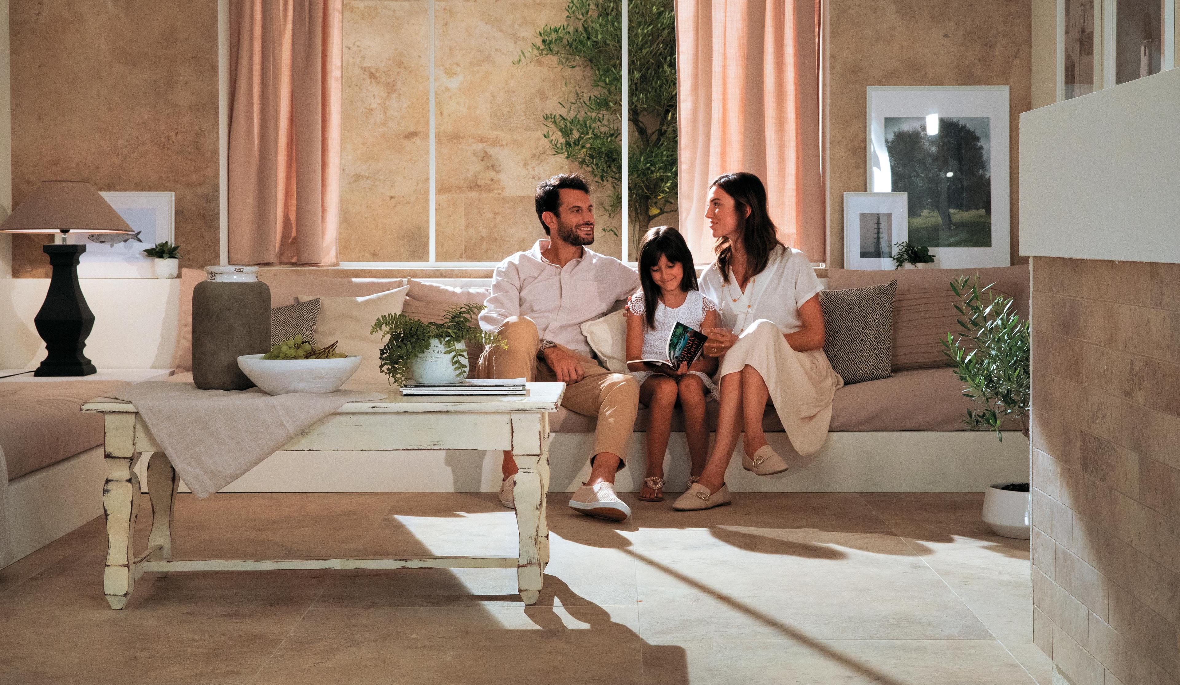 Famille assise dans un salon confortable avec sol en grès cérame effet pierre, table basse blanc antique et décorations naturelles.