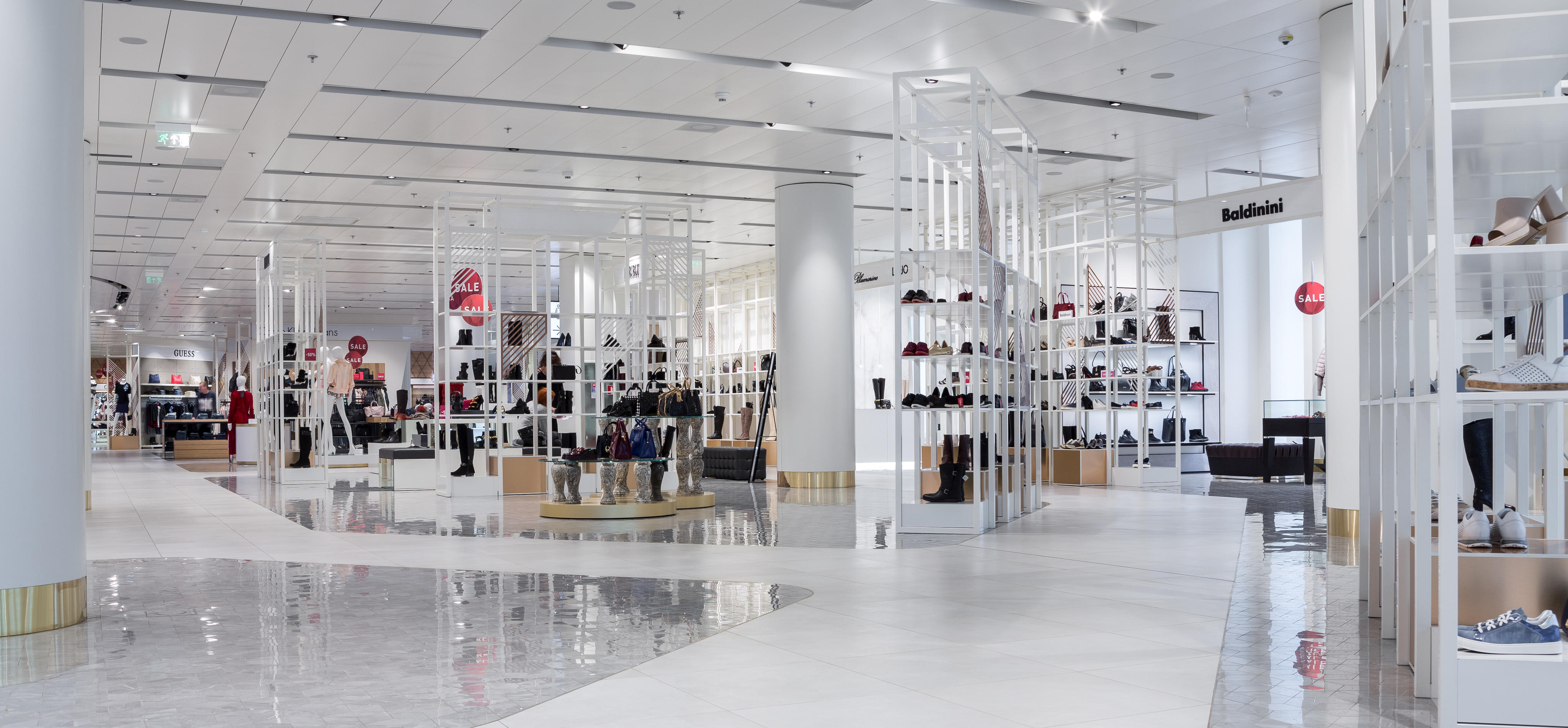 Interno di un centro commerciale moderno estetico con pavimenti lucidi, scaffali con scarpe e borse, e area di vendita illuminata.