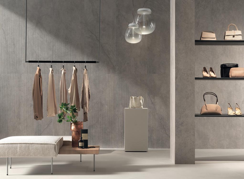 Modern shop with walls lined with gray 3D tiles, a coat rack with beige clothes, a bench and shelves with accessories.