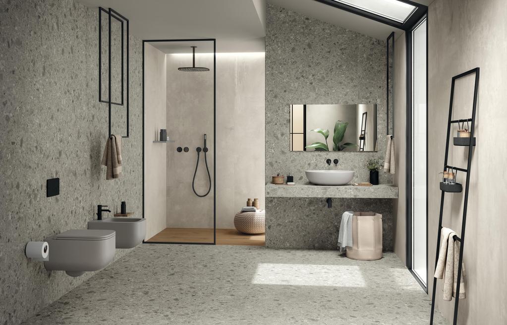 Modernes Bad mit Wänden und Boden in grauen Steinfliesen, Dusche mit Glastrennwand, hängenden Toiletten und weißem Waschbecken auf grauer Platte.