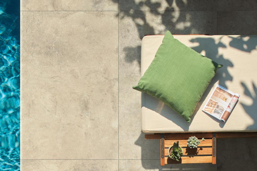 Piastrelle moderne per patio in gres porcellanato beige, cuscino verde su lettino e rivista.