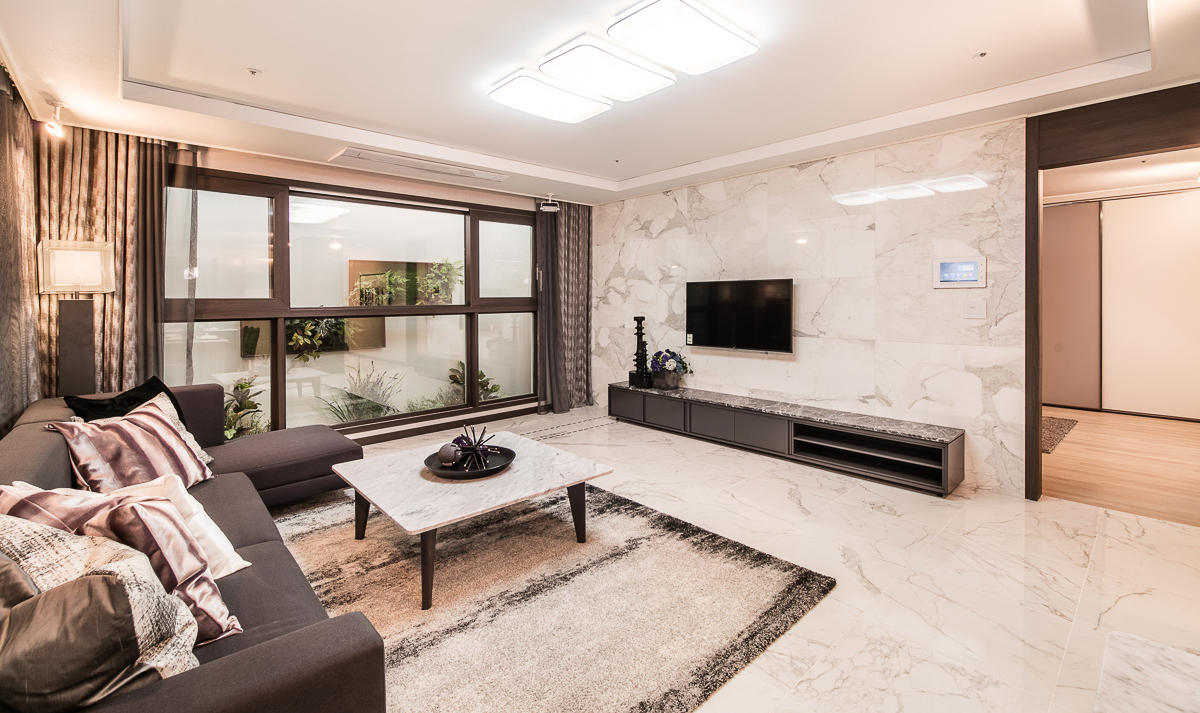 Salon d’un appartement coréen de luxe avec canapé d’angle, table en marbre, TV murale et sols en marbre.